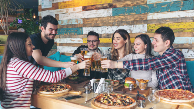 Happy young friends celebrating with pizza and drinking beer at bar restaurant